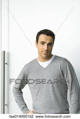 Stock Image - Man standing with hand on hip, looking at camera, portrait. Fotosearch