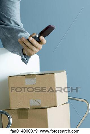 Man's hand holding cell phone, cardboard boxes piled on chair View Large Photo Image Stock Photo - Man's hand holding cell phone, cardboard boxes piled on chair. Fotosearch