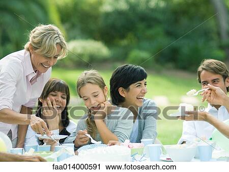 Stock Image - Outdoor birthday party, mature woman serving cake. Fotosearch