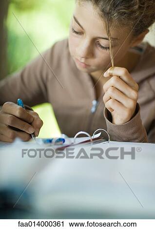 Stock Image - Preteen girl doing homework, twirling strand of hair. Fotosearch