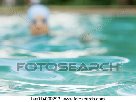 Stock Image - Surface of swimming pool water, swimmer in background. Fotosearch