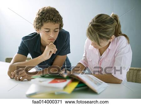 Stock Image - Teenage boy and girl doing homework together. Fotosearch