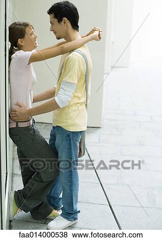 Stock Photo - Teenage couple standing with arms around each other, leaning against wall. Fotosearch