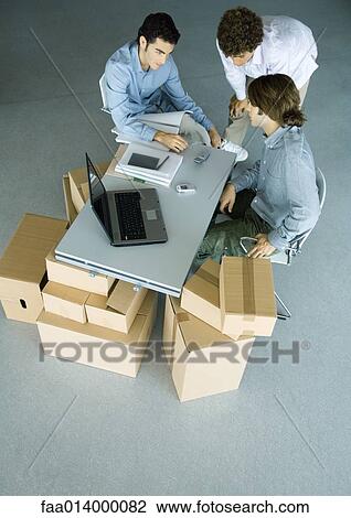 Three male colleagues grouped around cell phone on desk, surrounded by cardboard boxes View Large Photo Image Stock Image - Three male colleagues grouped around cell phone on desk, surrounded by cardboard boxes. Fotosearch