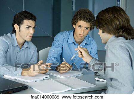 Three male colleagues sitting at table talking about documents View Large Photo Image Stock Photography - Three male colleagues sitting at table talking about documents. Fotosearch