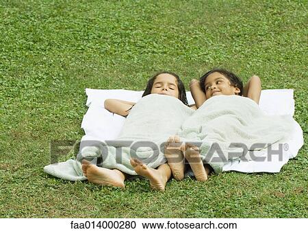 Two girls lying in grass, on a towel and covered with a towel View Large Photo Image Stock Image - Two girls lying in grass, on a towel and covered with a towel. Fotosearch