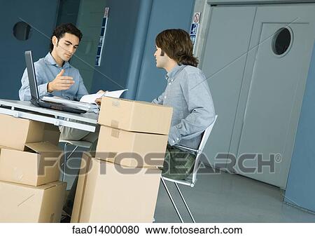 Two male colleagues talking across desk, cardboard boxes in foreground View Large Photo Image Stock Image - Two male colleagues talking across desk, cardboard boxes in foreground. Fotosearch