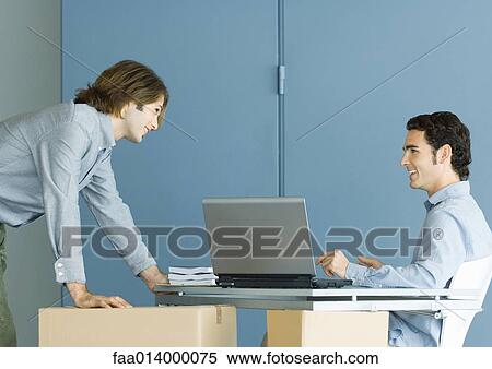 Two male colleagues talking across desk, cardboard boxes in foreground View Large Photo Image Stock Photography - Two male colleagues talking across desk, cardboard boxes in foreground. Fotosearch