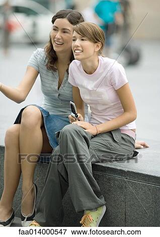 Two teenage girls sitting on bench in urban setting, laughing, one holding cell phone View Large Photo Image Stock Photo - Two teenage girls sitting on bench in urban setting, laughing, one holding cell phone. Fotosearch