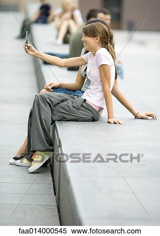 Two teenage girls sitting on bench in urban setting, taking photo with cell phone View Large Photo Image Stock Photography - Two teenage girls sitting on bench in urban setting, taking photo with cell phone. Fotosearch