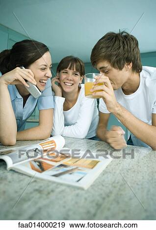 Stock Photo - Woman and adolescent children standing in kitchen together, talking. Fotosearch