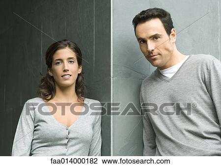 Stock Image - Woman and man leaning against corner of wall, looking at camera, portrait. Fotosearch