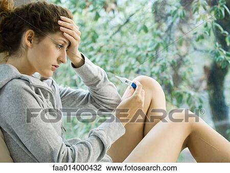 Woman holding head, looking at thermometer View Large Photo Image Stock Image - Woman holding head, looking at thermometer. Fotosearch
