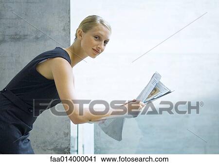 Stock Image - Woman leaning against glass guard rail, reading newspaper. Fotosearch