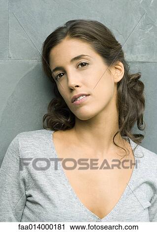 Stock Image - Woman leaning against wall, head and shoulders, portrait. Fotosearch