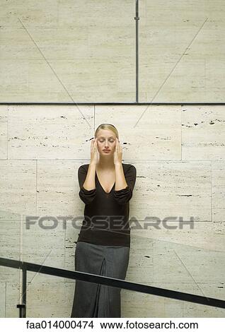 Woman leaning against wall, holding head, eyes closed View Large Photo Image Picture - Woman leaning against wall, holding head, eyes closed. Fotosearch