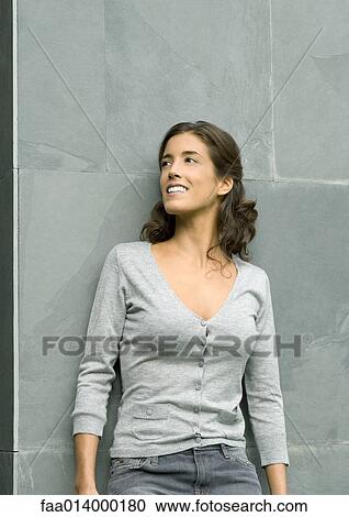 Stock Image - Woman leaning against wall, smiling, portrait. Fotosearch