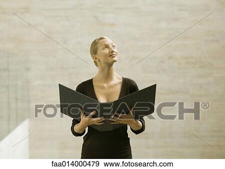 Woman standing holding open binder, looking away View Large Photo Image Stock Photo - Woman standing holding open binder, looking away. Fotosearch