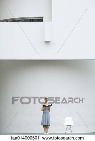 Woman standing next to chair, reading book View Large Photo Image Stock Image - Woman standing next to chair, reading book. Fotosearch