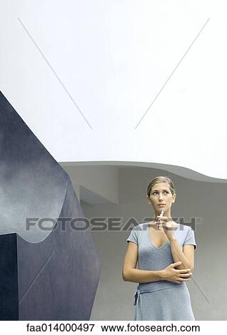 Woman standing next to sculpture, holding pen to chin View Large Photo Image Stock Photo - Woman standing next to sculpture, holding pen to chin. Fotosearch