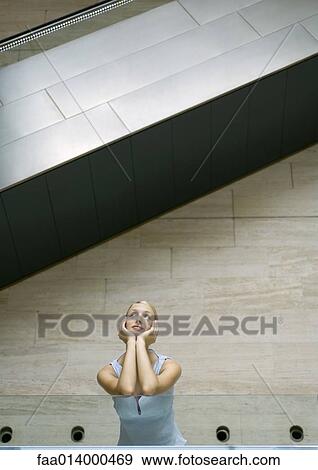 Stock Photo - Woman standing under escalator, leaning elbows on guard rail, low angle view. Fotosearch