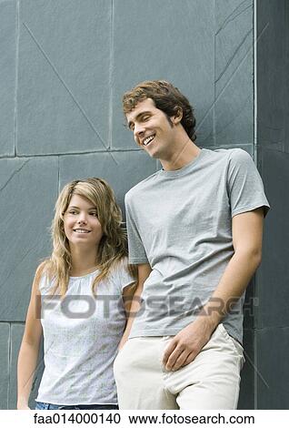 Young man and woman leaning against wall, smiling View Large Photo Image Stock Image - Young man and woman leaning against wall, smiling. Fotosearch