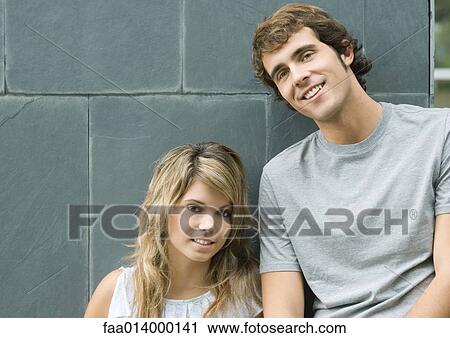 Young man and woman leaning against wall, smiling View Large Photo Image Stock Image - Young man and woman leaning against wall, smiling. Fotosearch