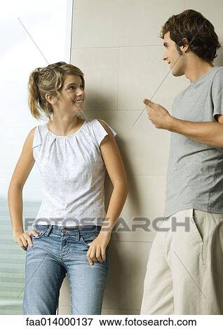 Stock Photo - Young man and woman leaning against wall, talking and smiling. Fotosearch