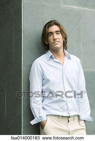 Young man leaning against wall with hands in pockets, looking at camera, portrait View Large Photo Image Stock Image - Young man leaning against wall with hands in pockets, looking at camera, portrait. Fotosearch