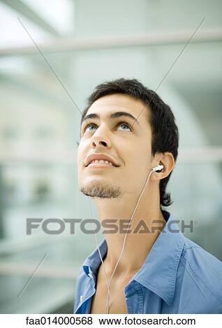 Young man listening to earphones, looking up View Large Photo Image Stock Photo - Young man listening to earphones, looking up. Fotosearch