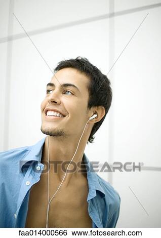 Young man listening to earphones, smiling View Large Photo Image Stock Photograph - Young man listening to earphones, smiling. Fotosearch