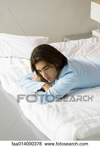 Young man lying on bed View Large Photo Image Stock Photo - Young man lying on bed. Fotosearch