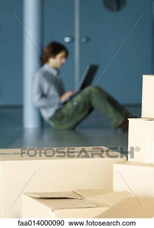 Young man sitting on floor using laptop, cardboard boxes in foreground View Large Photo Image Stock Image - Young man sitting on floor using laptop, cardboard boxes in foreground. Fotosearch