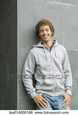 Stock Photo - Young man standing with thumbs in pockets, smiling at camera. Fotosearch