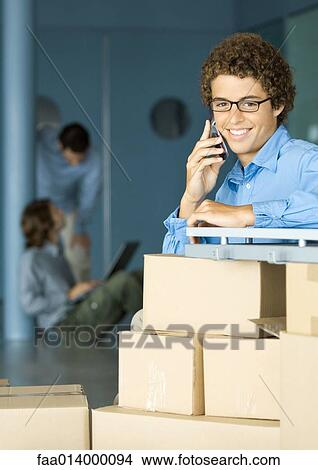Young man using cell phone, cardboard boxes in foreground View Large Photo Image Picture - Young man using cell phone, cardboard boxes in foreground. Fotosearch