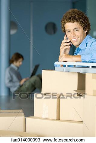 Young man using cell phone, cardboard boxes in foreground View Large Photo Image Stock Image - Young man using cell phone, cardboard boxes in foreground. Fotosearch
