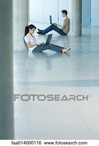 Stock Photograph - Young woman and man sitting on floor, using laptops. Fotosearch