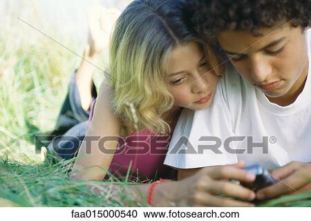 Boy and girl lying in grass, looking at cell phone View Large Photo Image Stock Image - Boy and girl lying in grass, looking at cell phone. Fotosearch