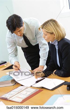 Stock Photo - Business colleagues, man leaning over woman's shoulder, pointing to documents. Fotosearch