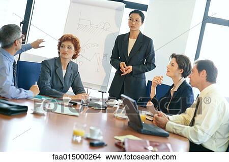 Business meeting, woman standing while man gestures toward flipchart View Large Photo Image Picture - Business meeting, woman standing while man gestures toward flipchart. Fotosearch