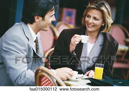 Stock Image - Businessman and woman sitting at sidewalk cafe, having coffee. Fotosearch