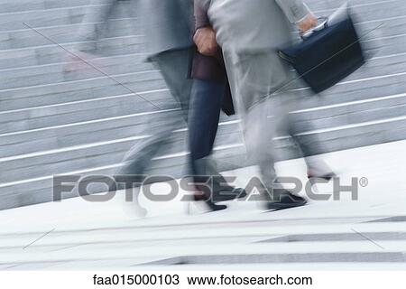 Stock Image - Businessman and woman walking, waist down, blurred motion. Fotosearch