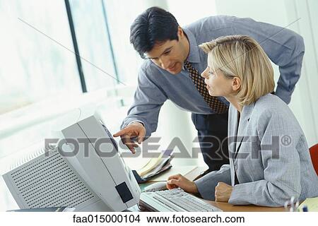 Businessman leaning over female colleague's shoulder pointing at monitor View Large Photo Image Picture - Businessman leaning over female colleague's shoulder pointing at monitor. Fotosearch
