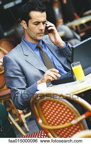 Businessman sitting in sidewalk cafe, using laptop and phone View Large Photo Image Stock Photograph - Businessman sitting in sidewalk cafe, using laptop and phone. Fotosearch