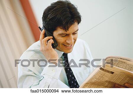 Businessman using phone and holding up financial section of newspaper View Large Photo Image Picture - Businessman using phone and holding up financial section of newspaper. Fotosearch