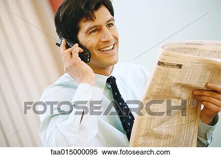 Stock Photography - Businessman using phone and holding up financial section of newspaper, smiling. Fotosearch