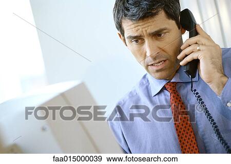 Businessman using phone, frowning and looking at computer View Large Photo Image Stock Photo - Businessman using phone, frowning and looking at computer. Fotosearch