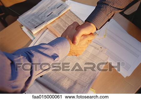 Businessmen shaking hands across table, cropped view, financial pages of newspapers in background View Large Photo Image Stock Image - Businessmen shaking hands across table, cropped view, financial pages of newspapers in background. Fotosearch