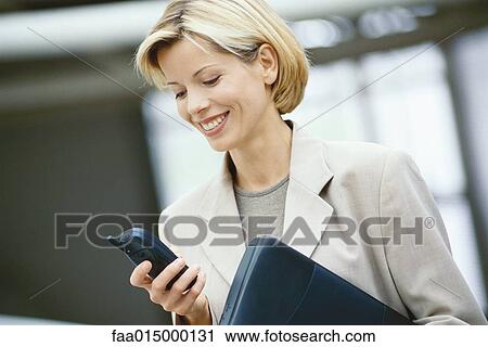 Businesswoman looking at phone, holding laptop View Large Photo Image Stock Image - Businesswoman looking at phone, holding laptop. Fotosearch