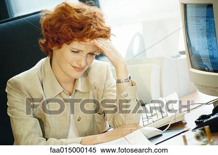 Stock Photography - Businesswoman sitting at desk, holding head. Fotosearch